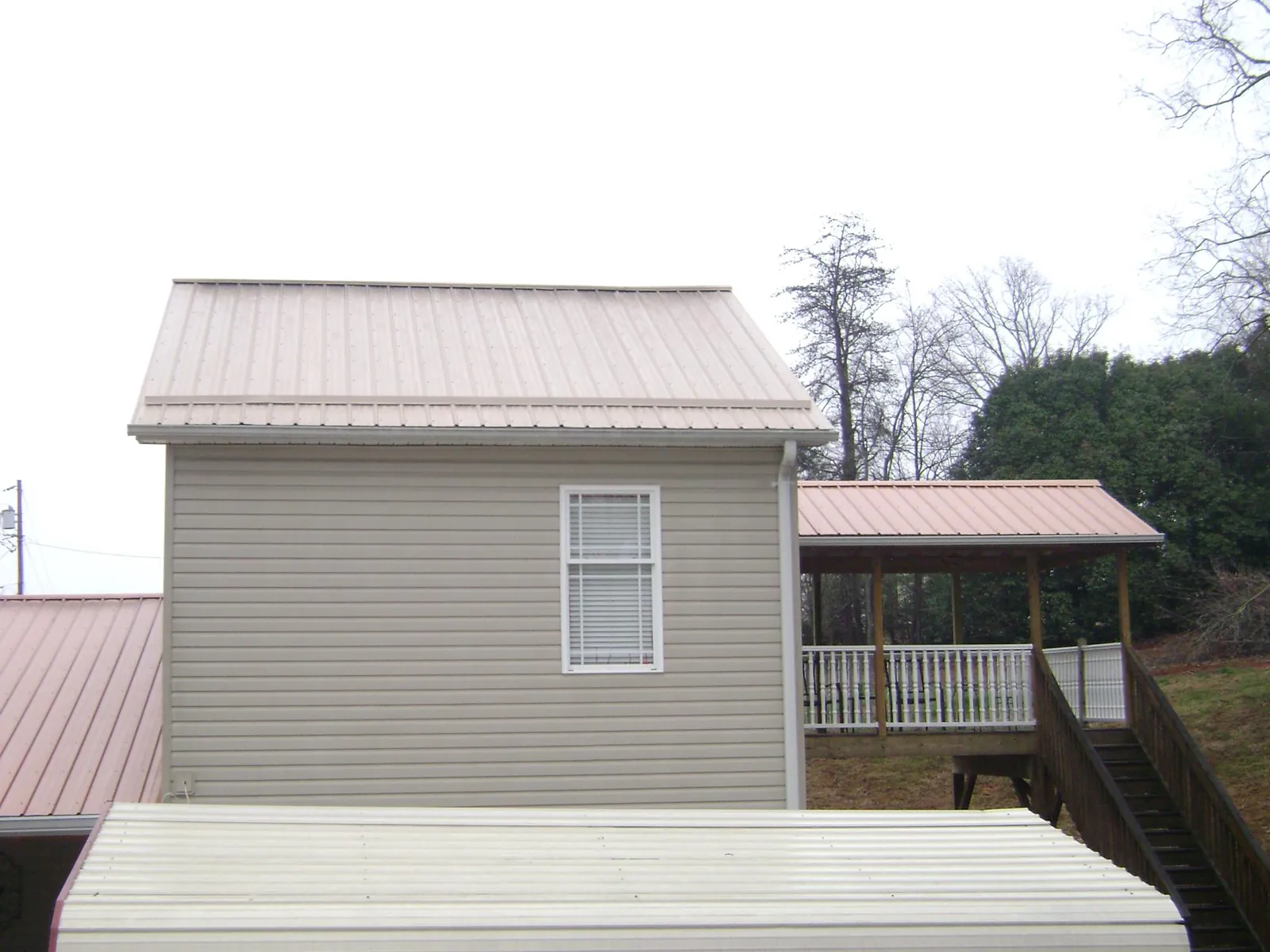 Tan metal roofs on a two story addition and attached porch, from a Roof Replacement job in Shirley